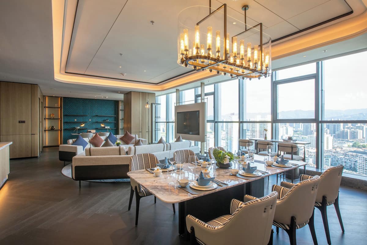 A modern dining area with a large table set for six, surrounded by comfortable seating. A large window offers a city view.