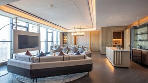 A modern living room with a large sectional sofa, a flat-screen TV, and a kitchen area with a bar. - Crowne Plaza Huaihua by IHG (Huaihua)