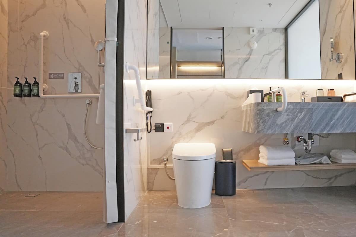 A modern bathroom with a marble floor, a toilet, a sink with a towel rack, and a mirror.
