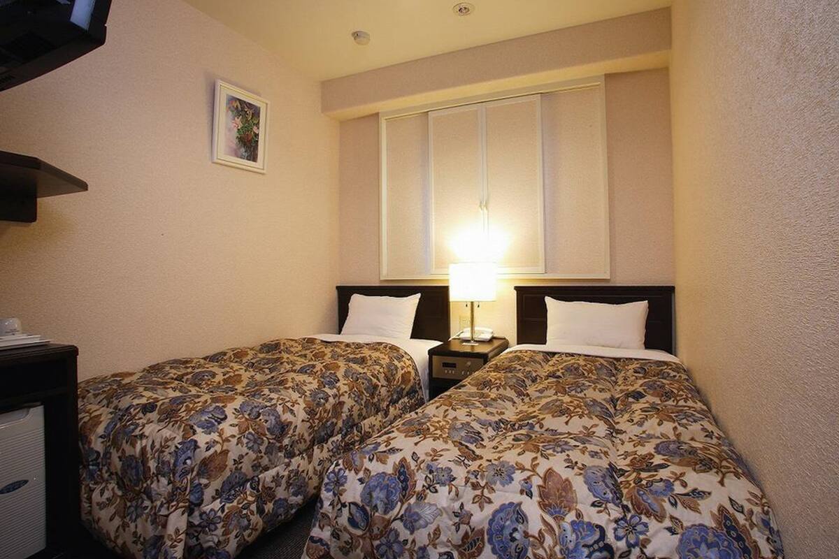 A hotel room with two beds, a nightstand with a lamp, and a small desk with a telephone.