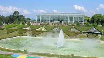 A large glass greenhouse surrounded by landscaped gardens and a central fountain.