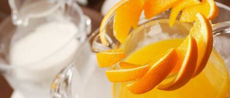 A glass pitcher and a glass with orange slices on a table.