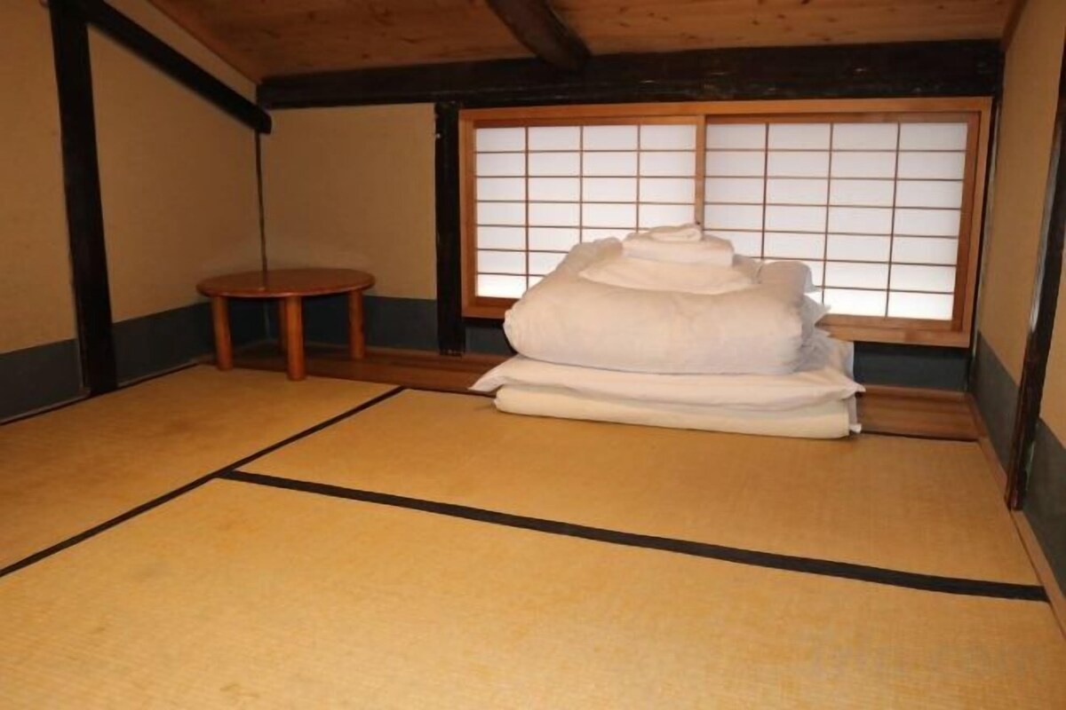 A tatami mat room with a traditional Japanese shoji screen, a small wooden stool, and a stack of white textiles.