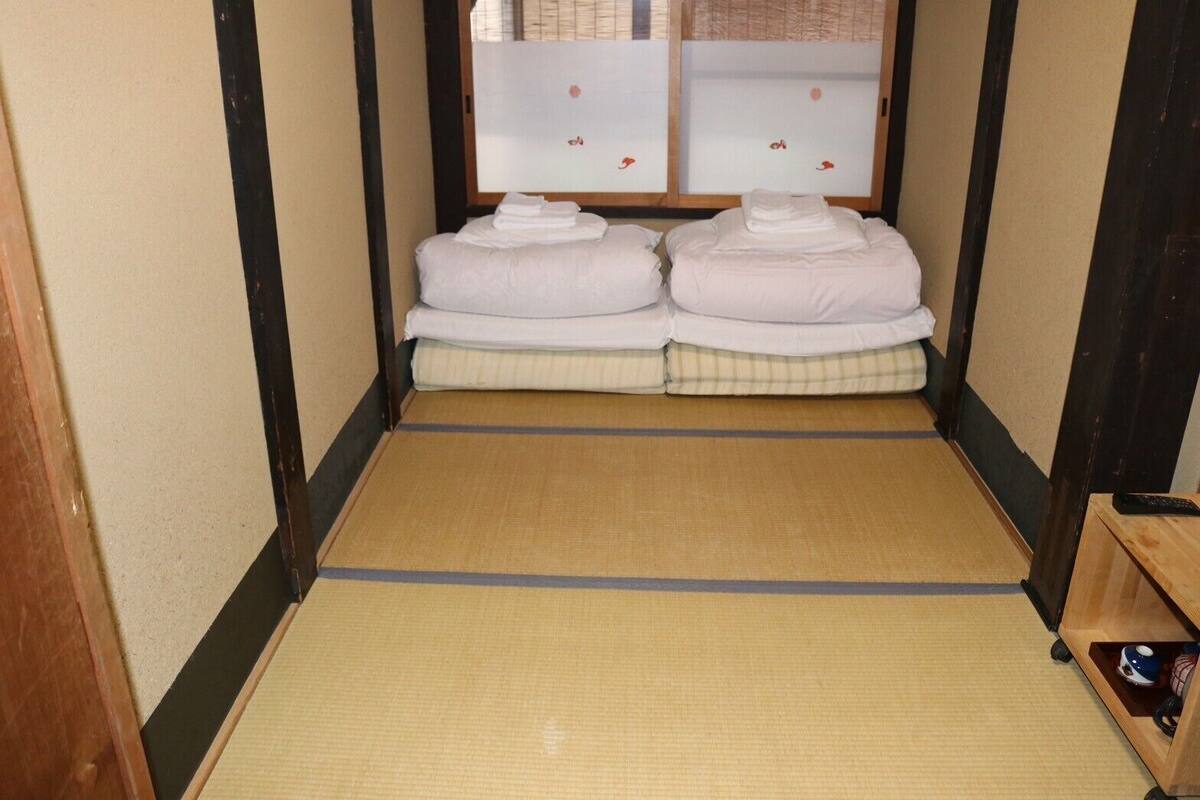 A traditional Japanese-style room with tatami flooring, two beds with white bedding, and a small wooden shelf with a kettle.