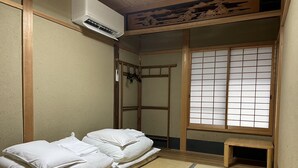 Ein traditioneller japanischer Raum mit Tatami-Bodenbelag, einer Futon-Liege, einem Shoji-Bildschirm und einer kleinen Holzbank.