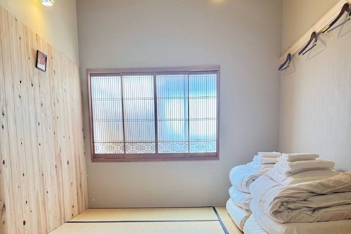 A room with tatami flooring, a shoji screen window, and a stack of towels on a shelf.