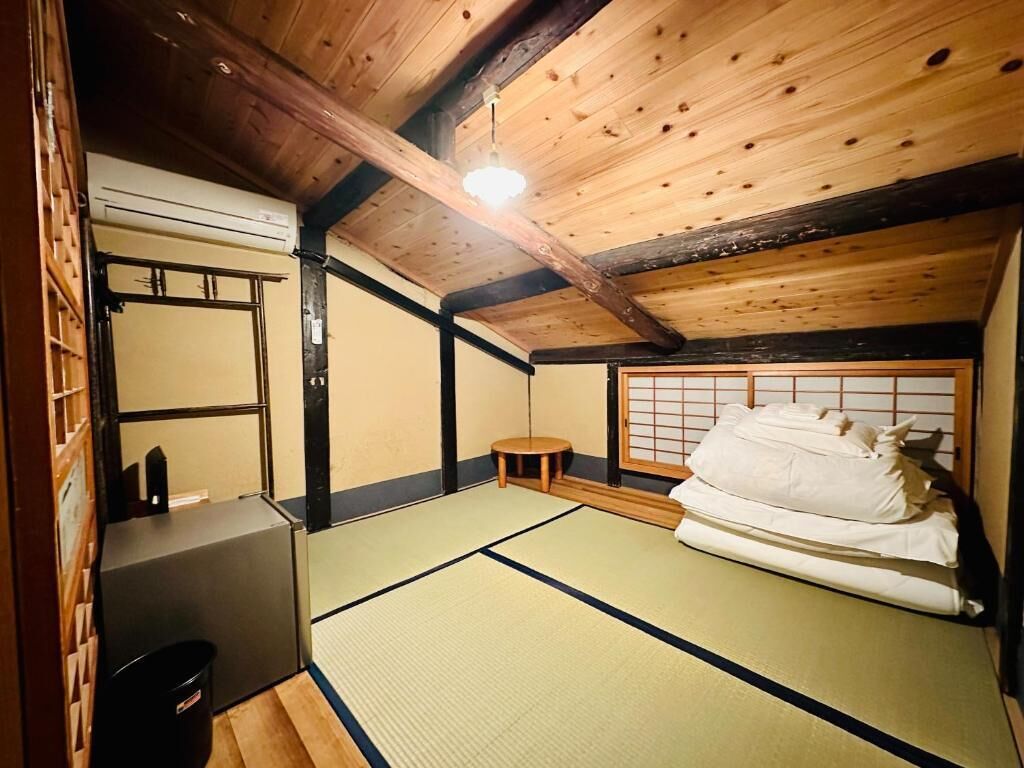 Una habitación japonesa tradicional con suelo de tatami, una cama futón, un mamparas shoji y techo de madera.
