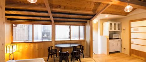Una habitación con techo de madera, una mesa de comedor con sillas, una cama, una ventana con persianas y una zona de cocina con armarios.