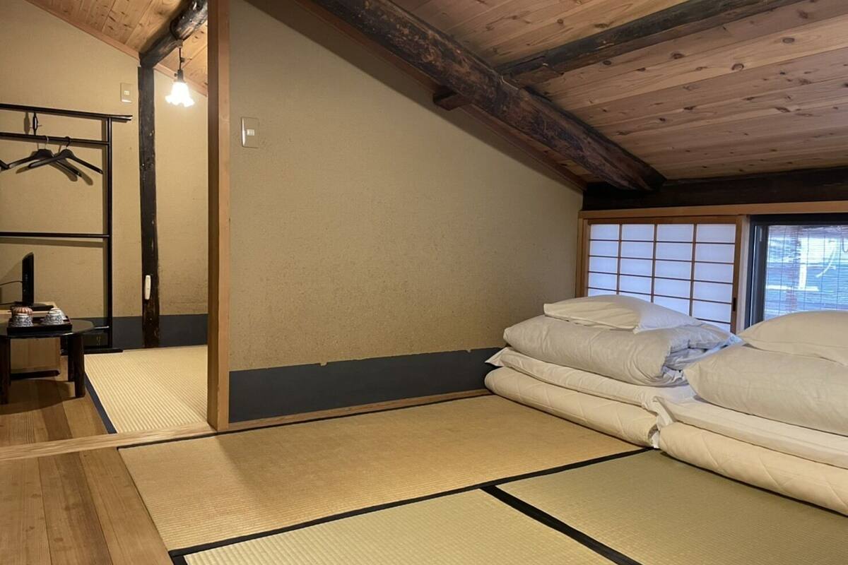 A traditional Japanese room with tatami flooring, a futon bed, a shoji screen, and a hanging clothes rack.