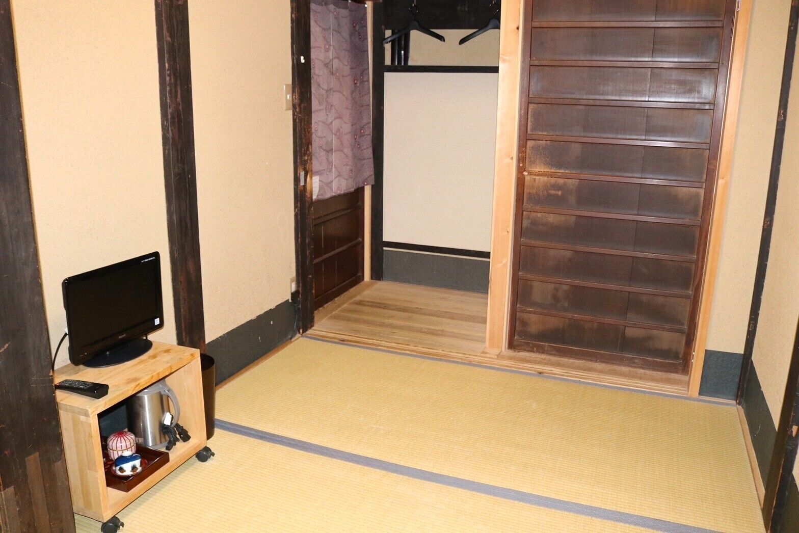 A room with a television on a wooden stand, a small table with a remote, and a sliding door.