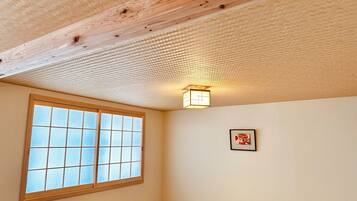 A room with a wooden ceiling, a window with a grid pattern, and a wall-mounted light fixture.