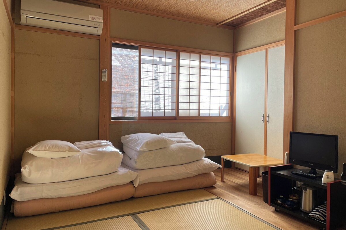 Quarto com futon, televisão e uma pequena mesa.