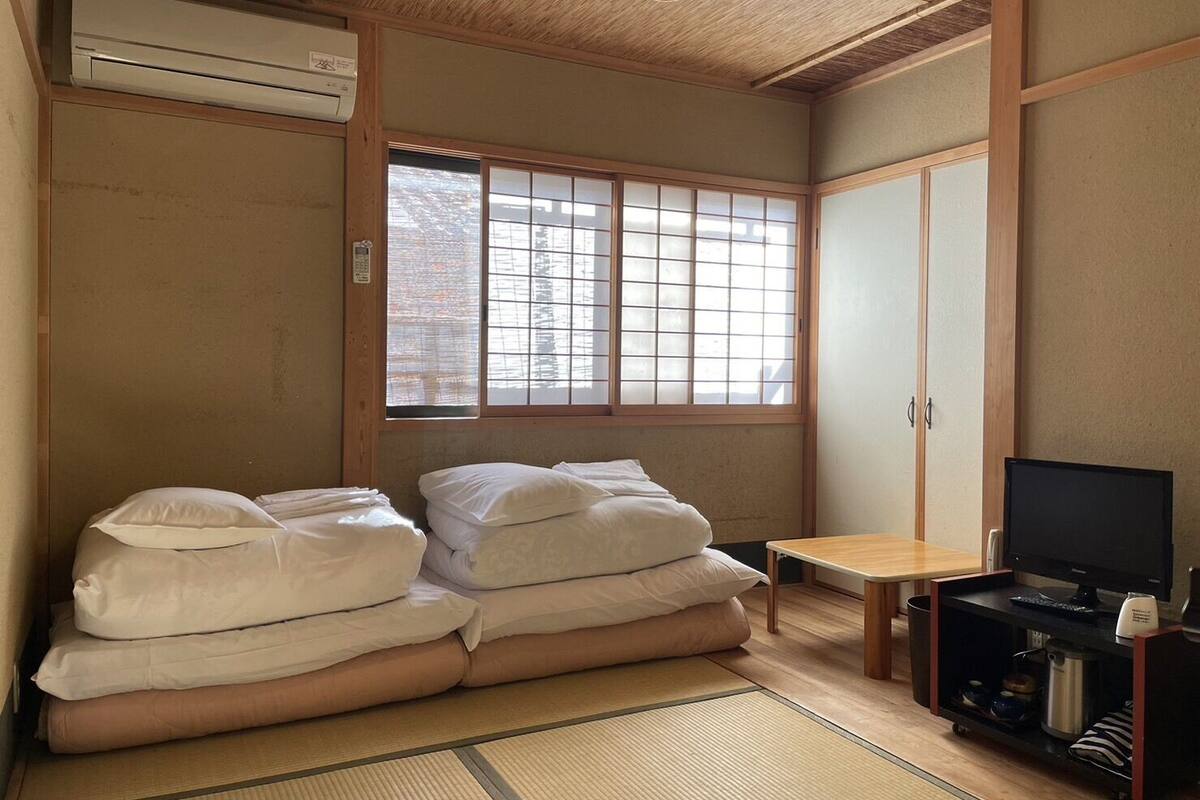A traditional Japanese-style room with tatami flooring, a futon bed, a television, and a sliding door.