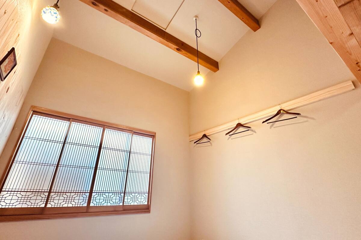 A room with a large window, wooden beams on the ceiling, and a few clothes hangers on the wall.