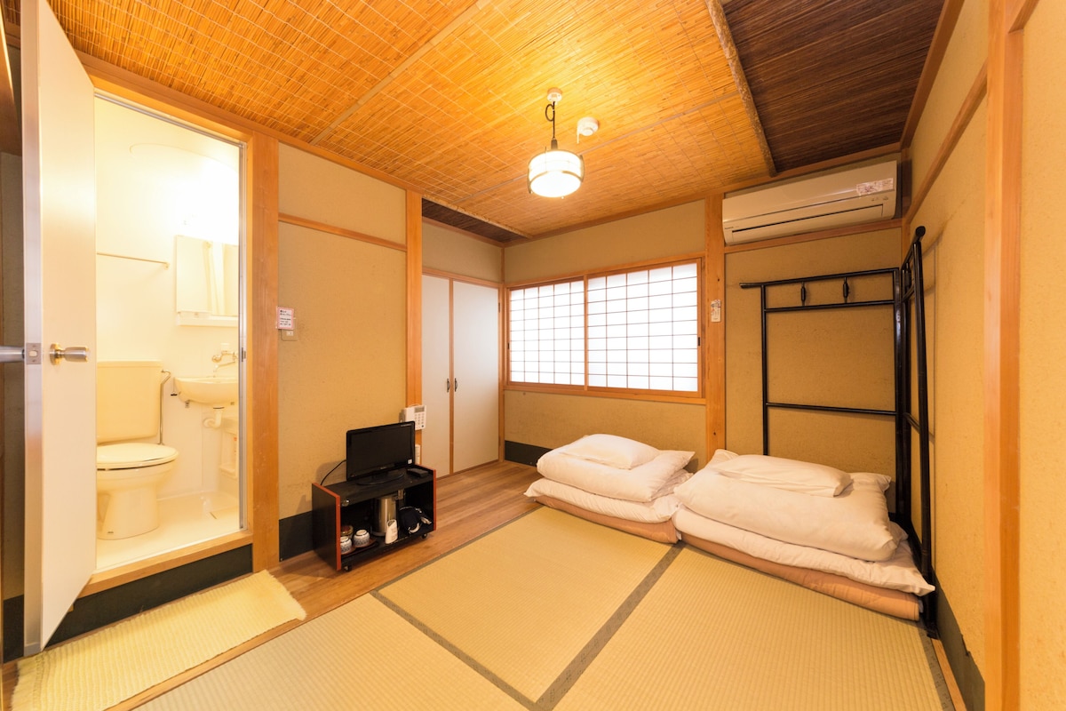 Een traditionele Japanse kamer met tatami vloeren, een futon bed, een wastafel en een schuifdeur naar een toilet.
