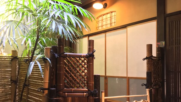 A traditional Japanese gate with bamboo construction, a bamboo fence, and a palm tree in the foreground.
