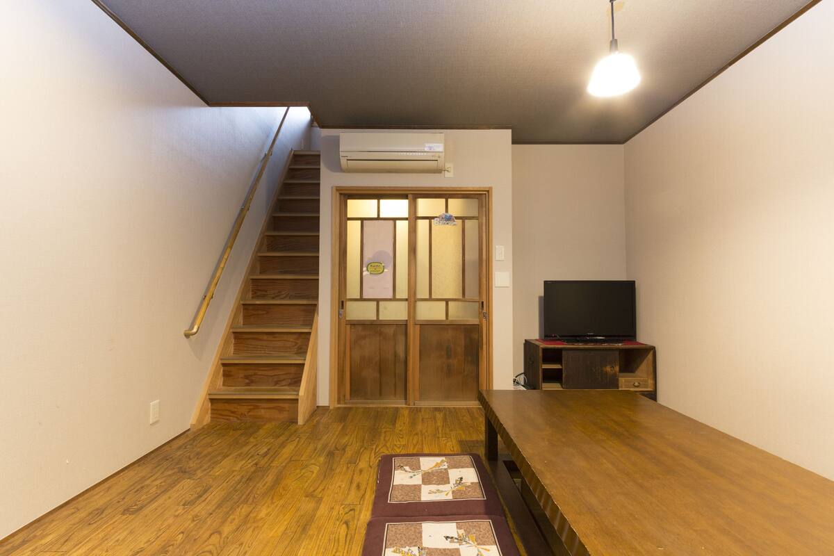A room with a wooden staircase, a television on a stand, and a tatami mat on the floor.