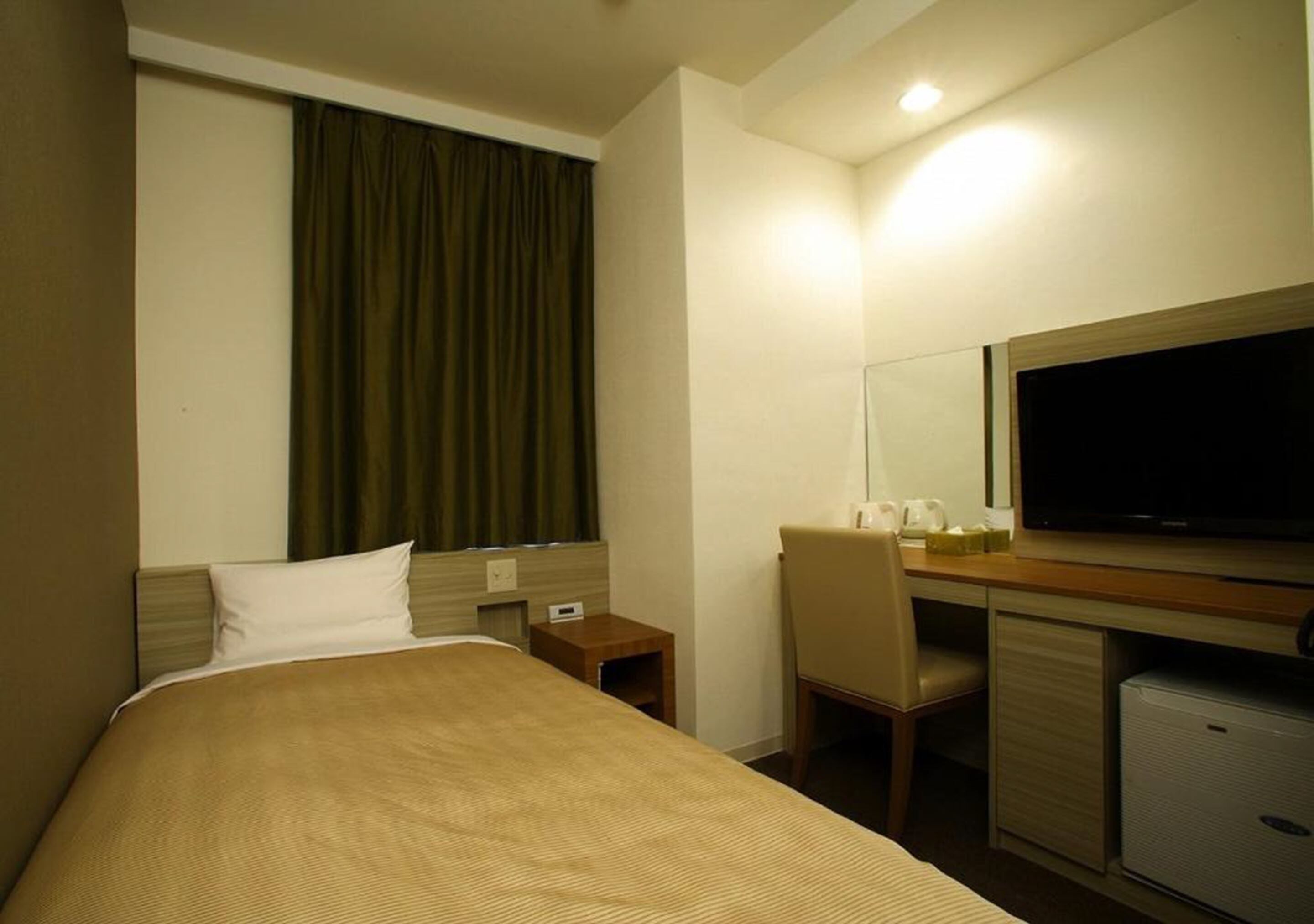 A hotel room with a bed, a desk with a chair, a television, and a small refrigerator.
