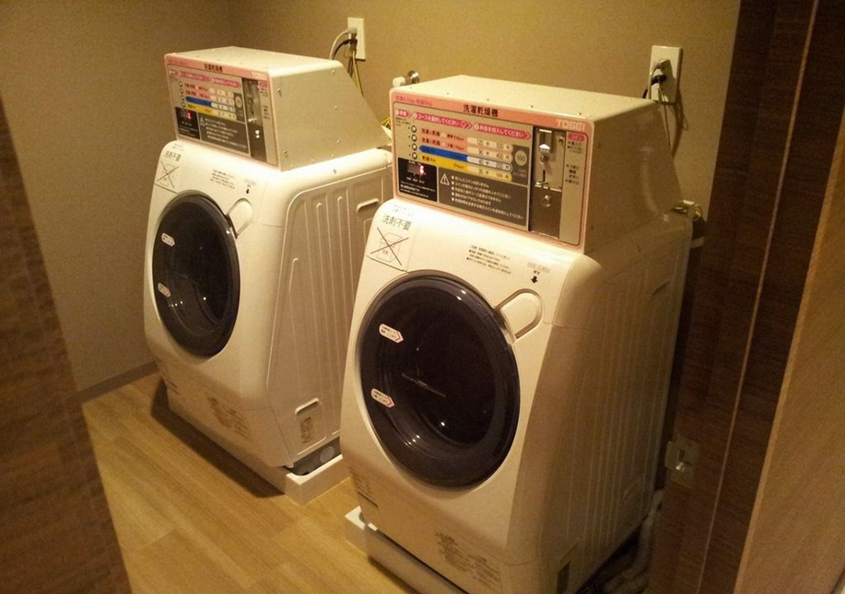Deux machines à laver à chargement frontal, superposées, dans une pièce dont le sol est recouvert de parquet.