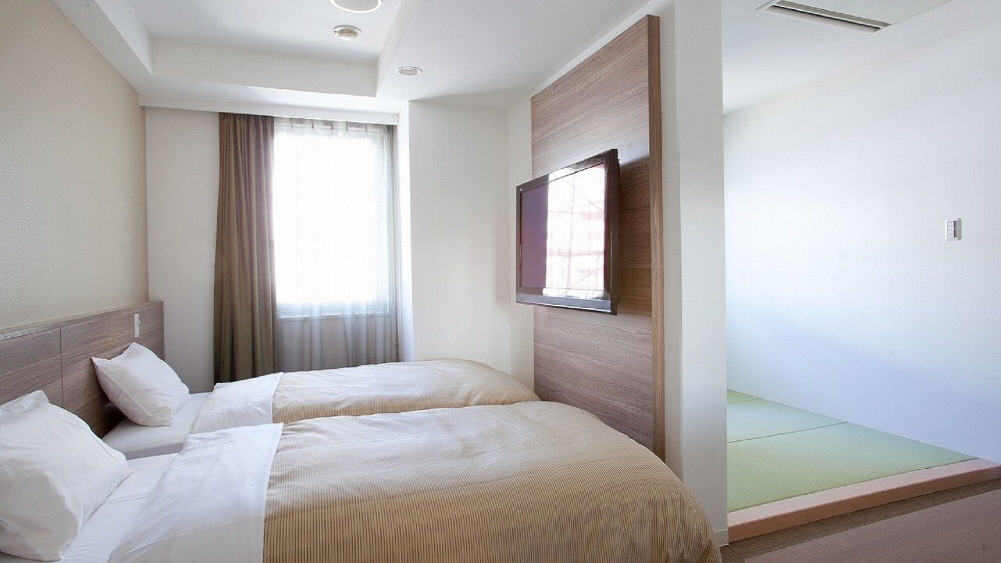 Une chambre d’hôtel avec deux lits, une grande fenêtre avec des rideaux, un téléviseur fixé au mur et un canapé vert.
