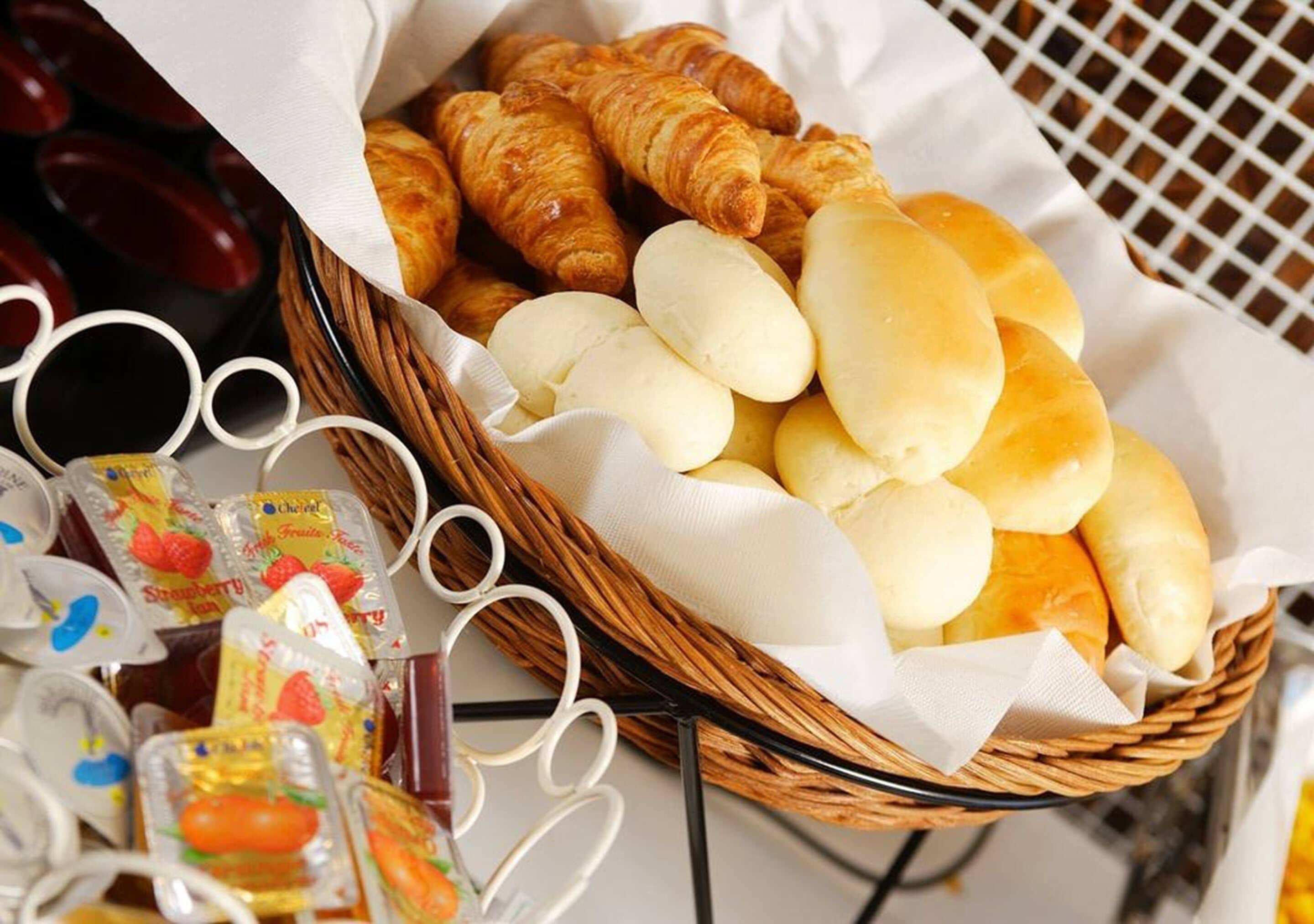 A basket containing croissants and bread rolls, with some packaged snacks visible in the background.