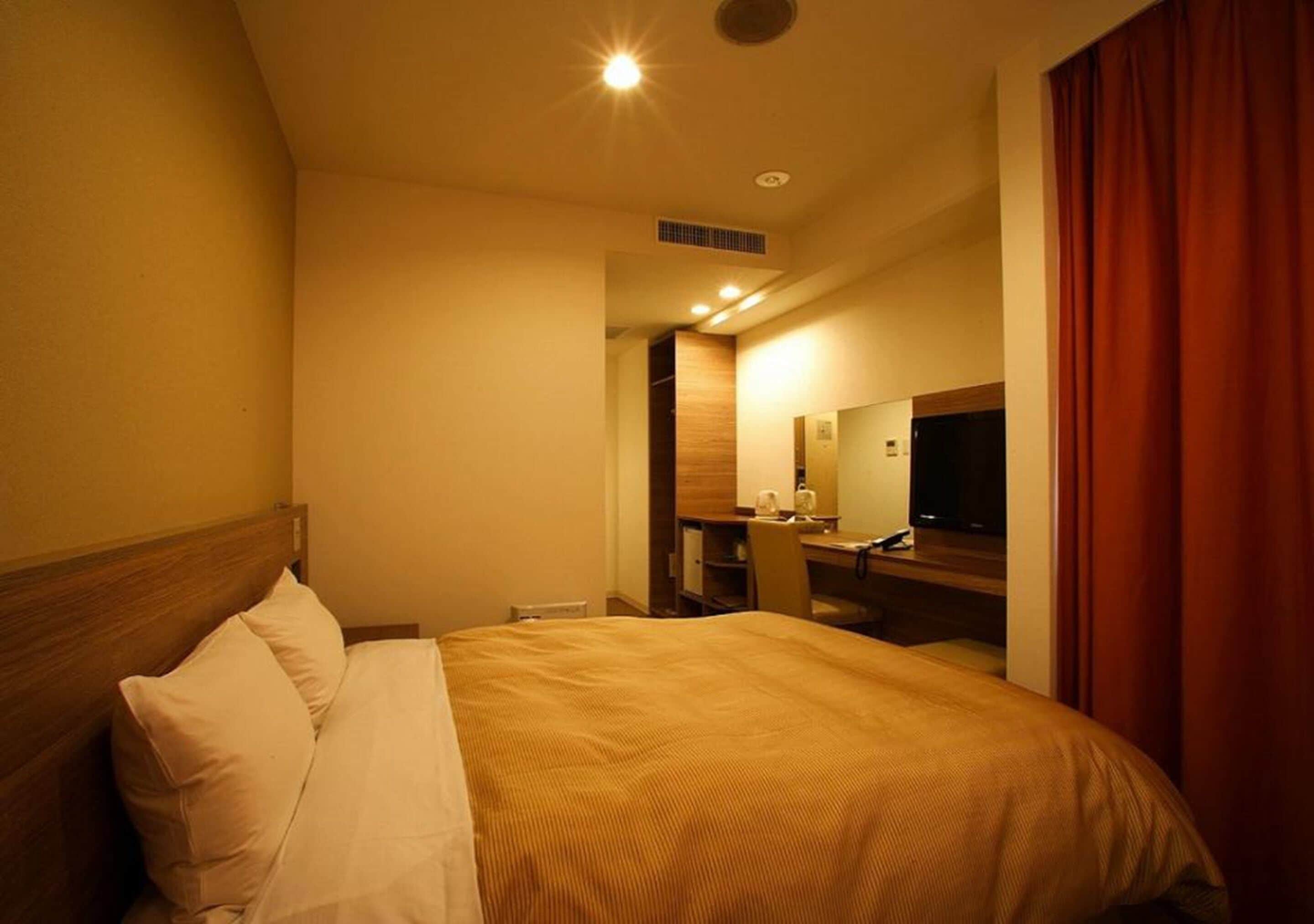 A hotel room with a bed, a desk, a chair, a television, and a mirror.