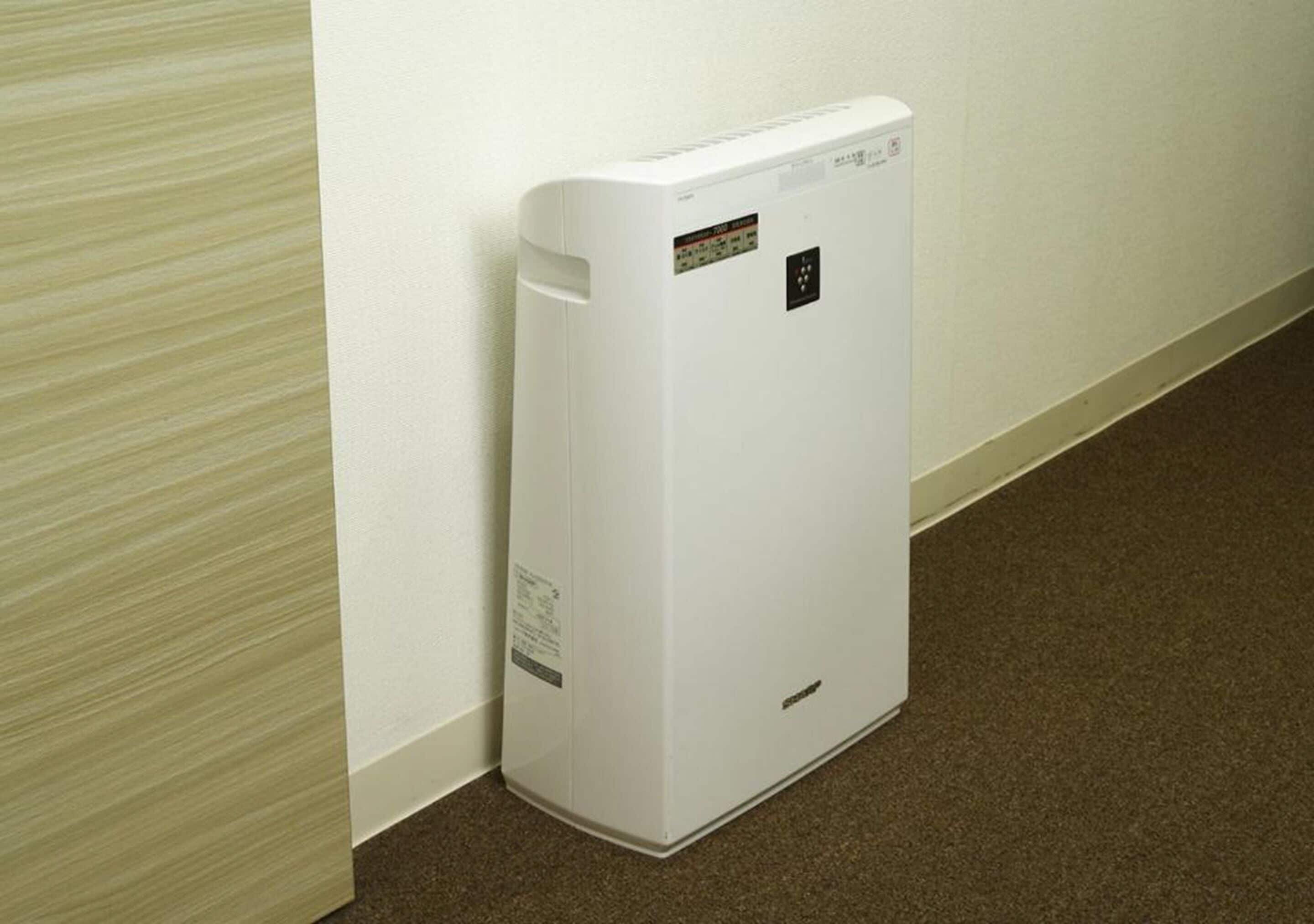 A white portable heater against a wall with a carpeted floor.