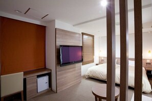 Een moderne hotelkamer met een flatscreen televisie aan de muur, een bed met witte beddengoed, een klein nachtkastje en een ronde tafel.