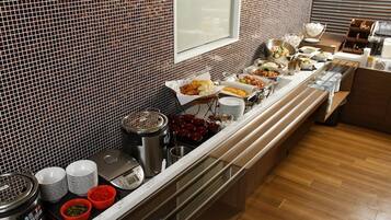 A buffet setup with various food items and condiments, a window, and a tiled wall.