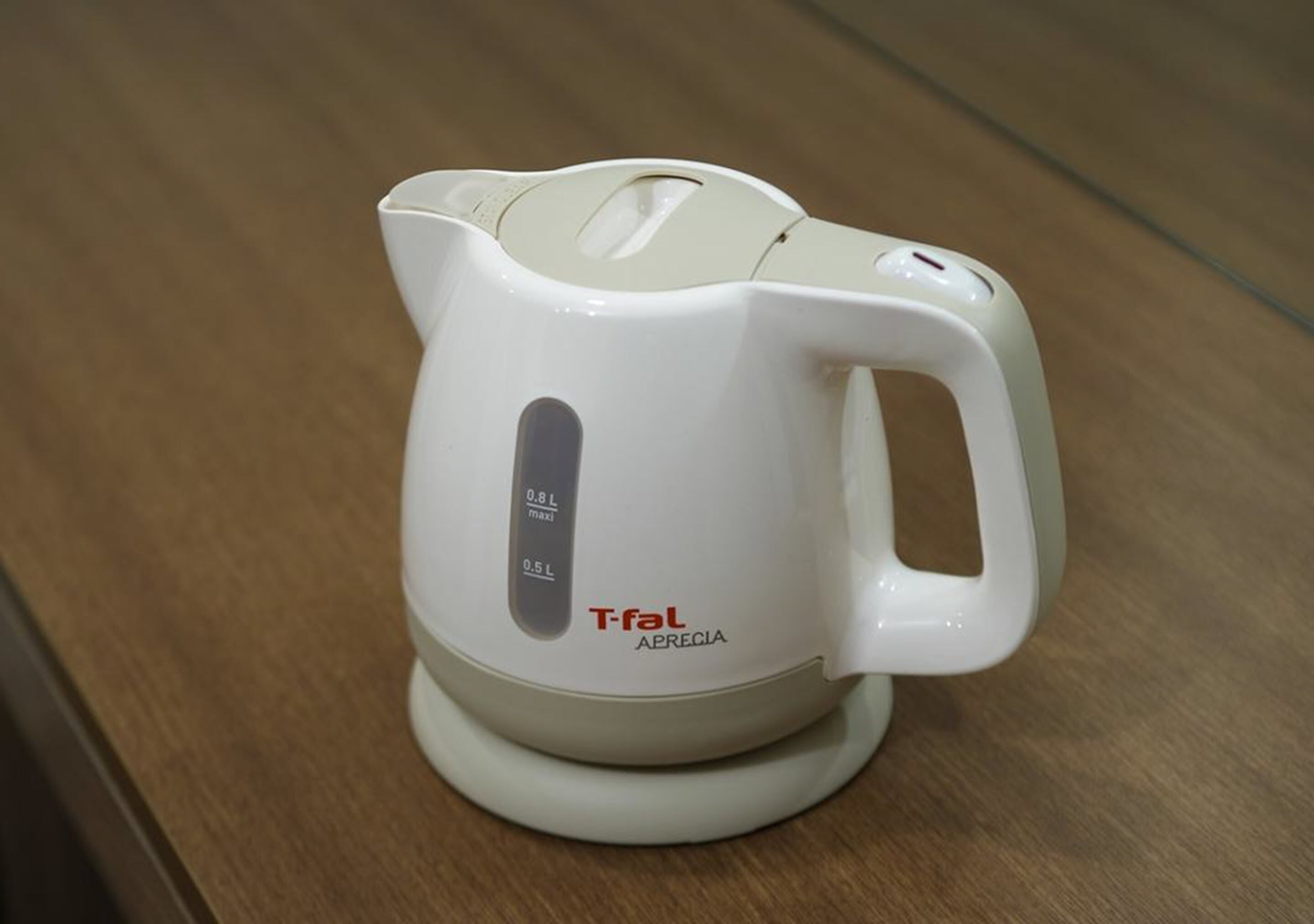 A white electric kettle with a handle and a spout, placed on a wooden surface.