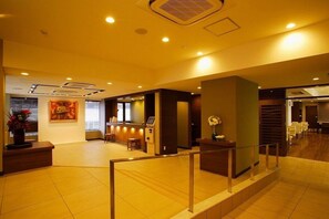 Een hotel lobby met een receptiebalie, een zithoek en een trap.