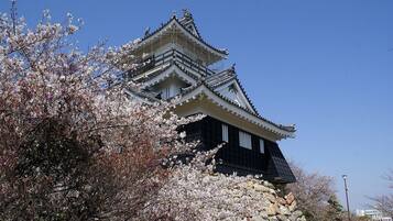 A traditional Japanese castle with multiple tiers and a stone base, surrounded by cherry blossoms.
