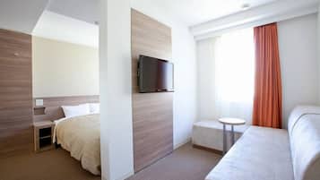 A modern hotel room with a bed, a TV mounted on a wooden panel, a small round table, and a sofa.