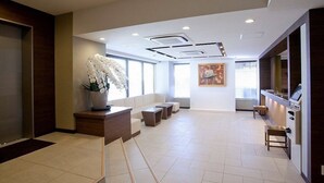 Un hall d’hôtel moderne doté d’un comptoir d’accueil, d’un espace salon et d’une grande fenêtre laissant entrer la lumière naturelle.