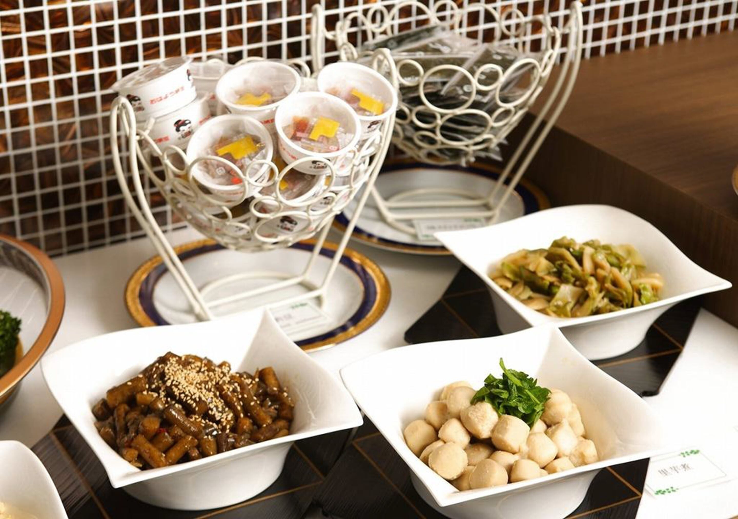 Una mesa con diversos platos en cuencos blancos, una cesta de metal con tazas y un rebozo de azulejos.