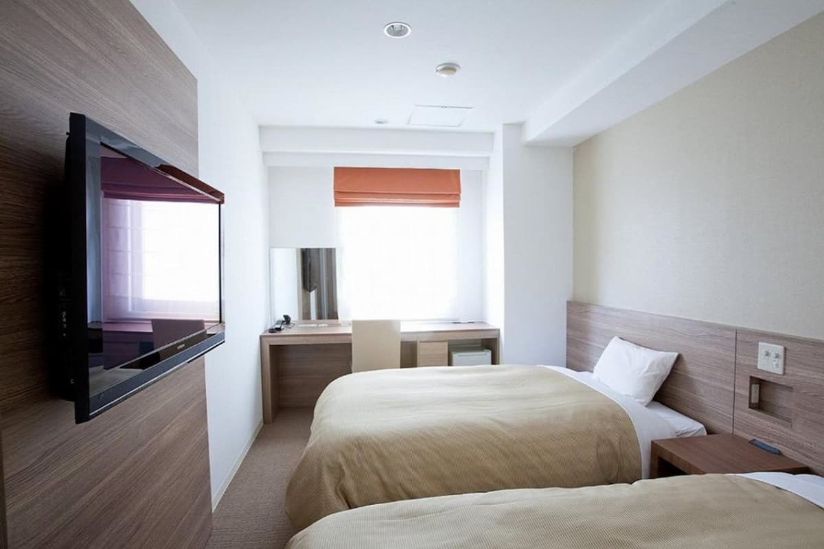 Een hotelkamer met twee bedden, een aan de muur bevestigde televisie, een bureau met stoel en een raam met verduistering.