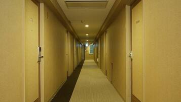 A hotel hallway with doors on both sides, a carpeted floor, and a ceiling with recessed lighting.