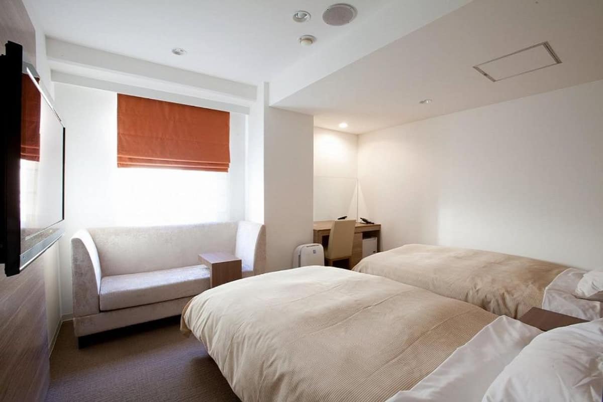 Een hotelkamer met twee bedden, een bank, een bureau en een lamp.