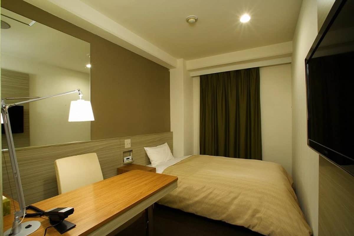 Een hotelkamer met een bed, een bureau met lamp, een televisie en een raam met gordijnen.