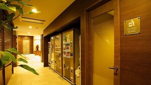 Un couloir d’hôtel avec des machines à laver à pièces, une porte en bois et une plante.