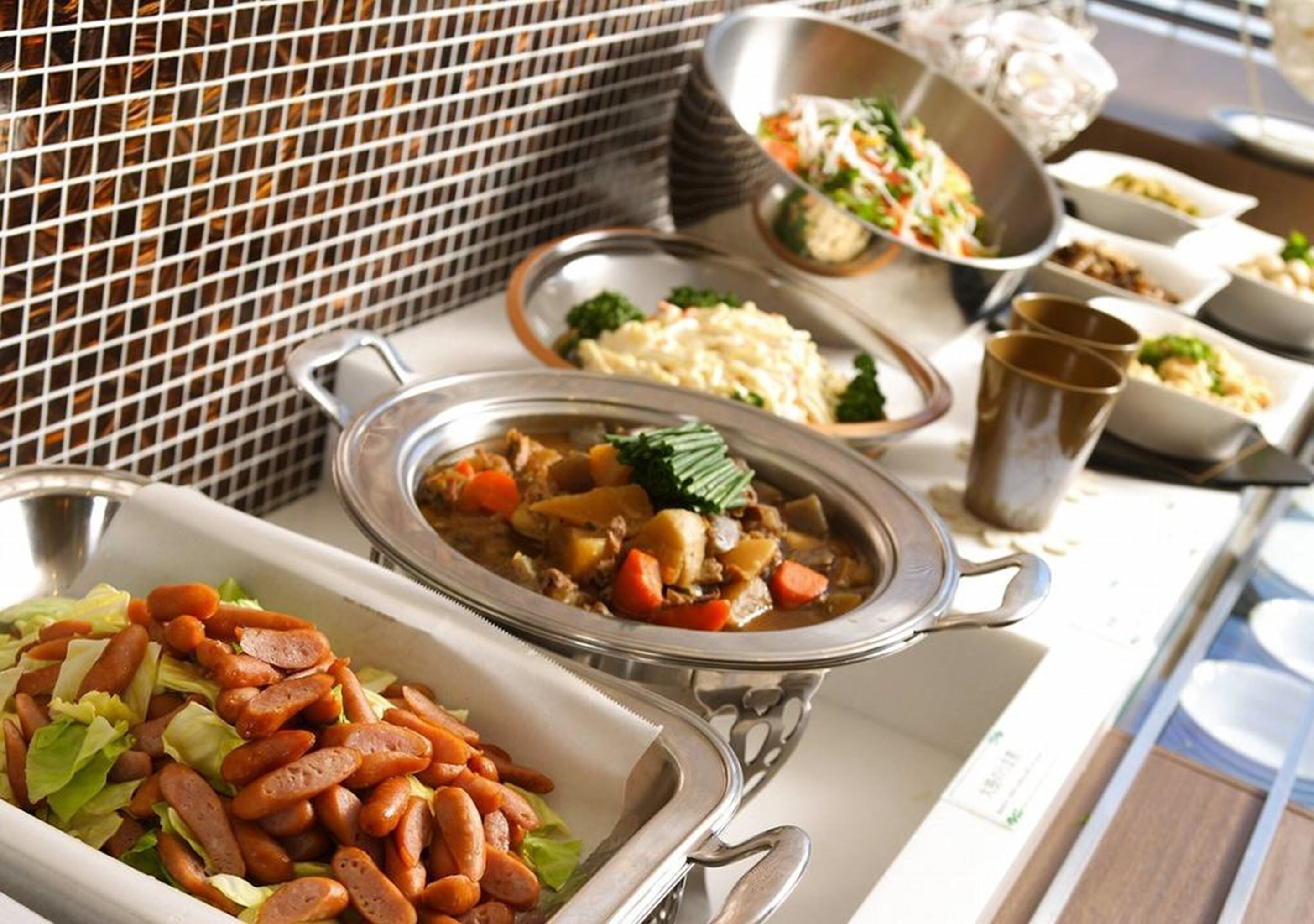 A buffet table with various dishes including a pot of stew, a salad, and a dish with sausages.