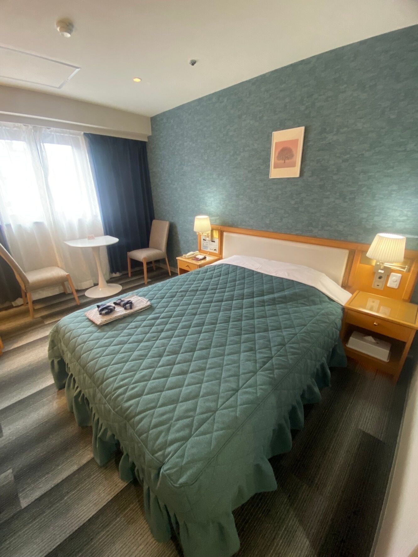 Habitación de hotel con una cama grande, una silla, una mesita y una mesita de noche con una lámpara.