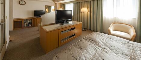 Una habitación de hotel con una cama, televisión, escritorio, silla y lámpara.