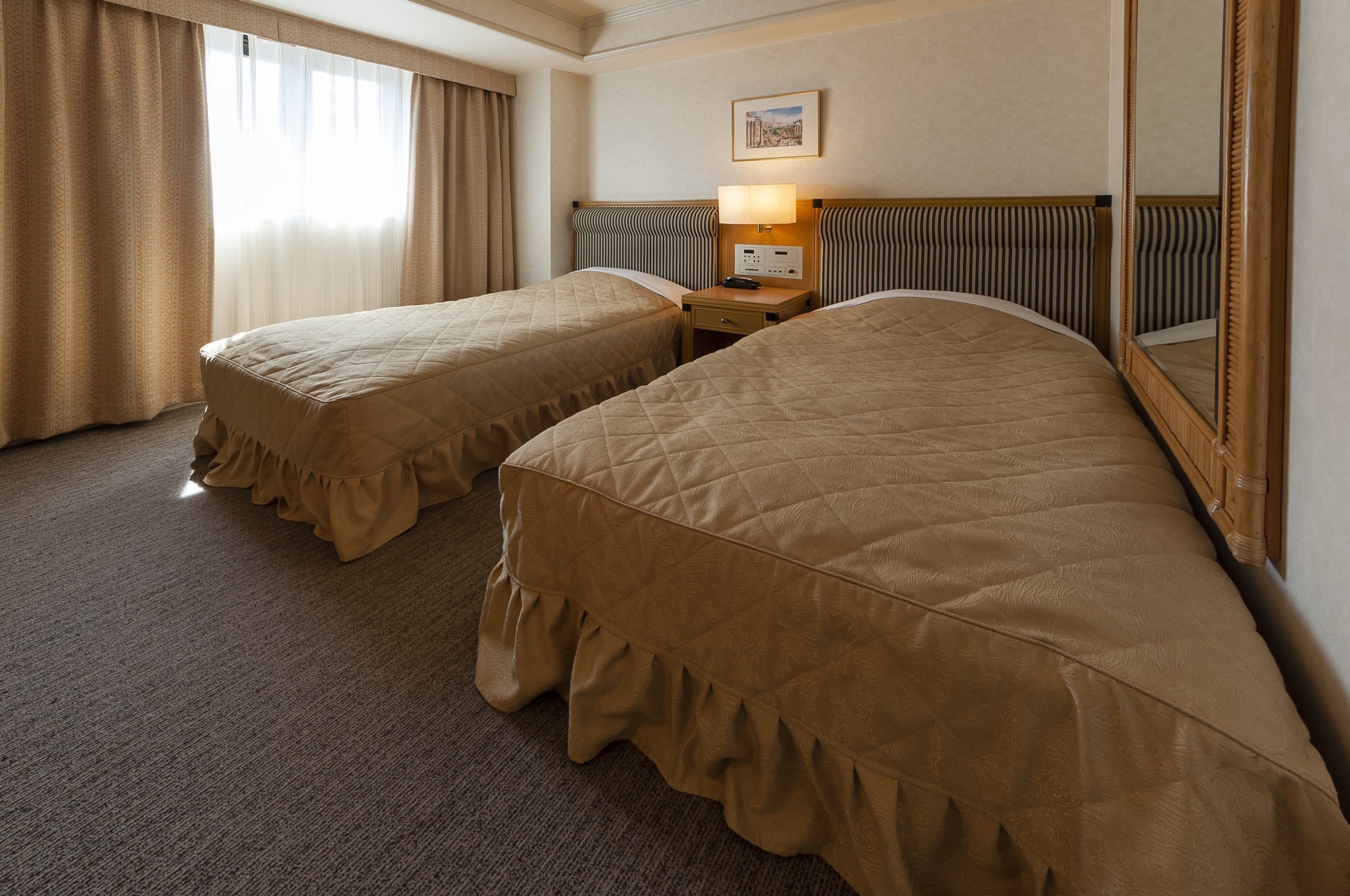 A hotel room with two beds, a nightstand with a lamp, a mirror, and a framed picture on the wall.