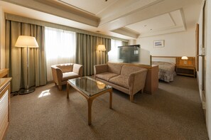 A hotel room with a sofa, armchair, glass coffee table, and a bed with a nightstand. - Hotel Siena (Tokyo)