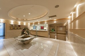 A hotel lobby with a reception desk, a glass coffee table with a floral arrangement, and a staircase leading to the upper floor. - Hotel Siena (Tokyo)