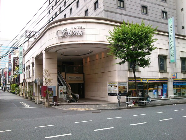 A hotel entrance with a curved facade, an escalator, and a sign indicating the hotel name. - Hotel Siena (Tokyo)