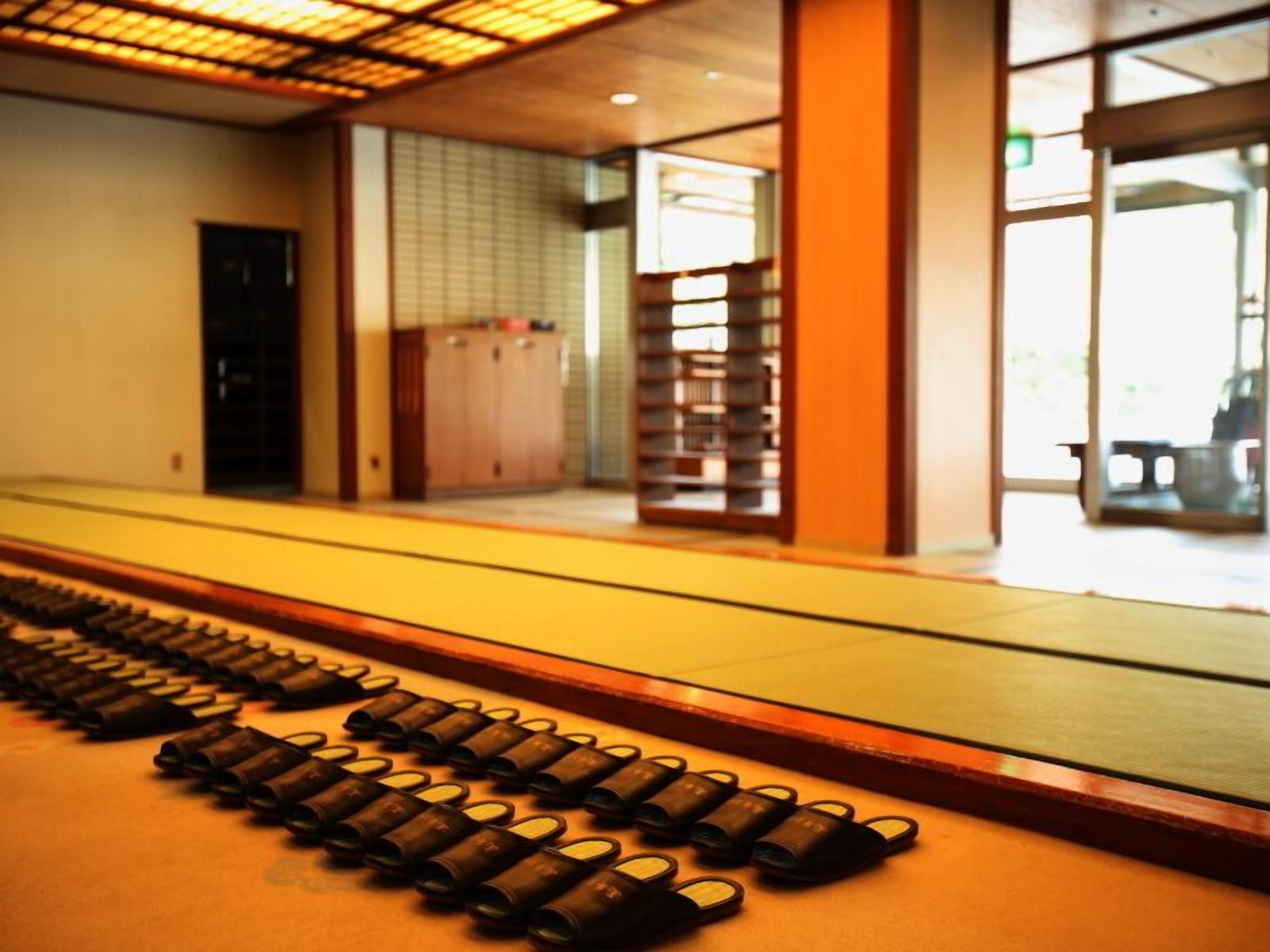 A corridor with a series of cylindrical objects arranged in a line, a wooden door, and a view into a room with a tiled wall and a bench.