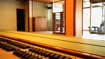 A corridor with a series of cylindrical objects arranged in a line, a wooden door, and a view into a room with a tiled wall and a bench.
