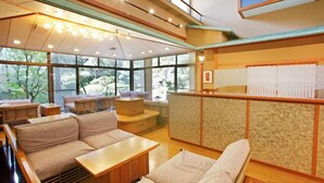 Un intérieur moderne avec un coin salon, des meubles en bois et de grandes fenêtres donnant sur un paysage verdoyant.